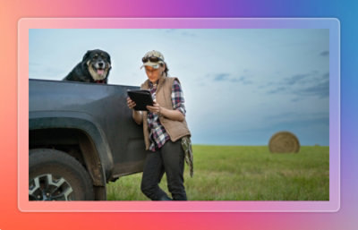 Two people standing beside a pickup truck in an open field, reviewing information on a tablet near farm equipment.