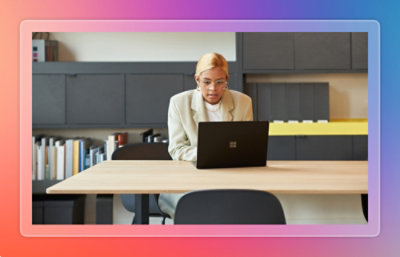 Professional working on a laptop at a long table in a library‑style workspace.
