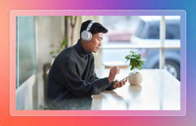 Person wearing headphones using a phone at a table with a plant.