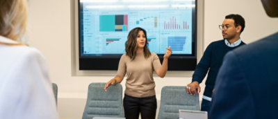 Team presenting and discussing charts on a screen during a meeting in a conference room.