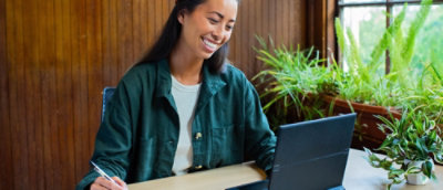 Person working at desk with laptop and notebook in a plant‑filled workspace