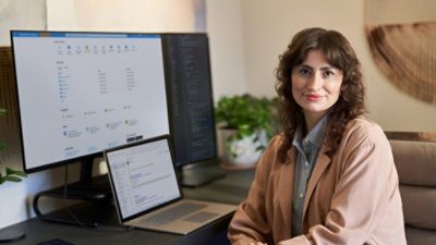 Person sitting at a desk with a laptop and large monitor displaying software dashboards in a modern workspace.