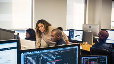  Two people coding on computers in a room full of monitors