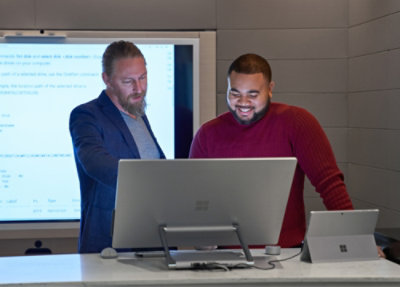 A couple of men standing in front of a computer.