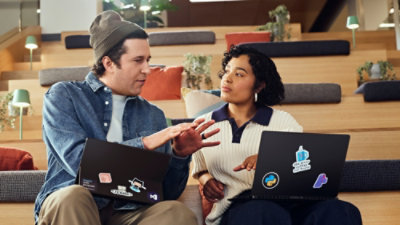 Two people discussing while using laptops in a communal workspace