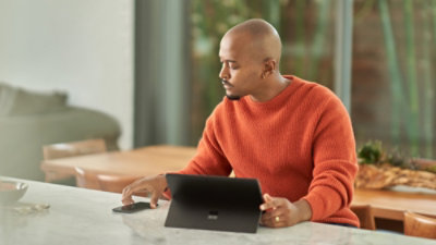 Person seated at a table, using a tablet, with a notebook and pen nearby.