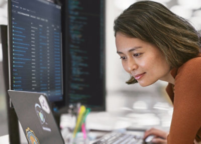 Person working on a laptop with multiple code screens in an office.