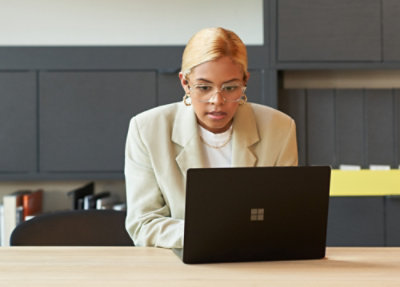 A woman wearing glasses and a white jacket working on a laptop.
