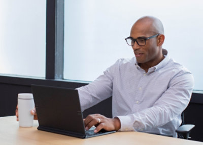 Person working on a laptop at a desk in a modern office, holding a coffee cup beside the computer.