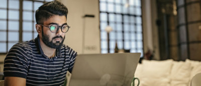 A man wearing glasses and a striped shirt looking at a laptop.