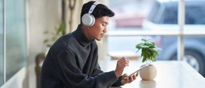 A person wearing headphones and using a tablet at a table with a potted plant.