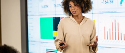 Presenter explaining insights in front of a large screen displaying charts and data visualizations.