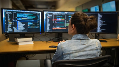 A woman looking at code on multiple screens