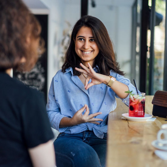 Woman sitting at a table in a cafe signing to another person.