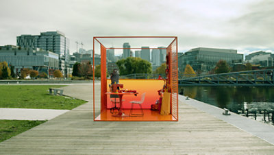 Ein kleiner, futuristischer und farbenfroher Bürowürfel inmitten eines Parks am Rande einer Großstadt.