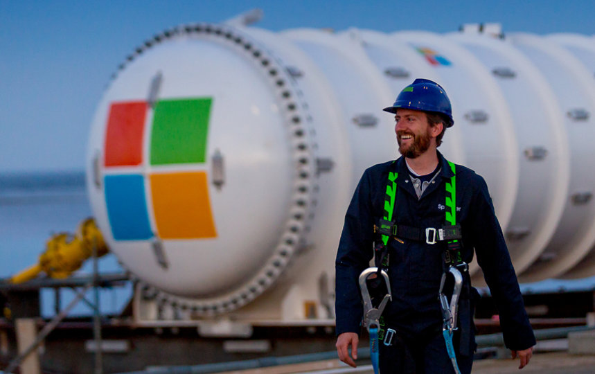 Ein lächelnder Fabrikarbeiter vor einem Gastank mit einem Microsoft Logo.