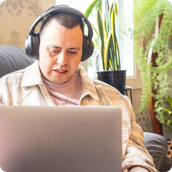 Young adult with autism looking at laptop with headphones on.