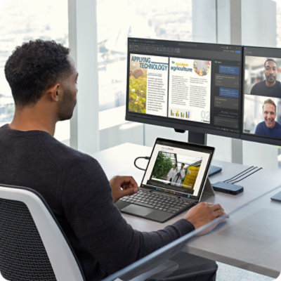 Man in a modern high-rise office sitting at a desk with multiple monitors connected to a Surface Pro featuring Live Captions.