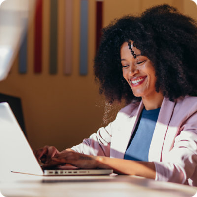 Cheerful African American businesswoman sitting at desk typing on laptop, working in modern office.