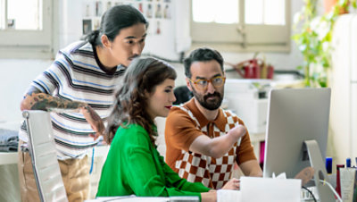 In an office, three people, one of whom has a physical disability, look at a monitor.