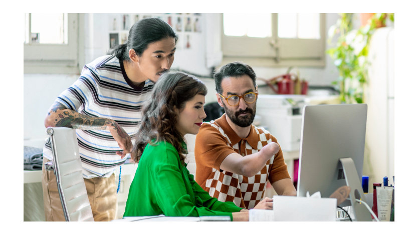 En una oficina, tres personas, una de ellas con discapacidad física, miran un monitor.