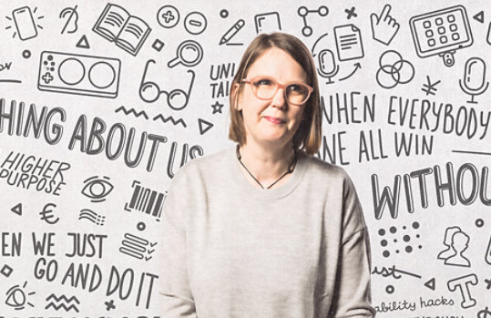 Jenny Lay-Flurrie em pé na frente de uma parede com palavras e ilustrações