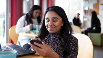 Pessoa sorrindo enviando uma mensagem de texto enquanto usa um laptop em um refeitório.