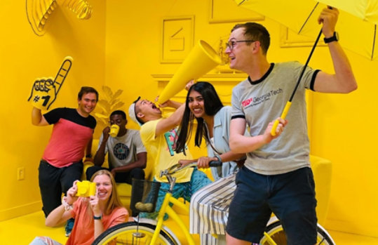 Grant recipient Mentra team members in fun room painted yellow holding various yellow objects.