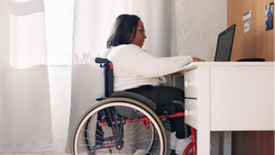 A young woman using a wheelchair in front of her laptop.