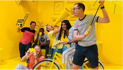 Various Mentra teams in fun room painted yellow while holding various yellow objects.