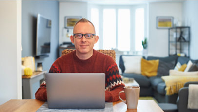 A man sits in front of his laptop in the living room, staring forward.