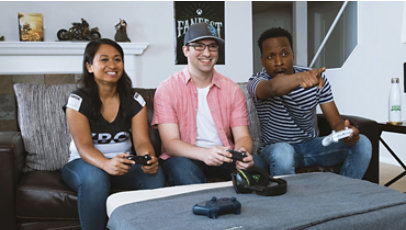 Tres personas juegan felizmente con una Xbox en un salón.