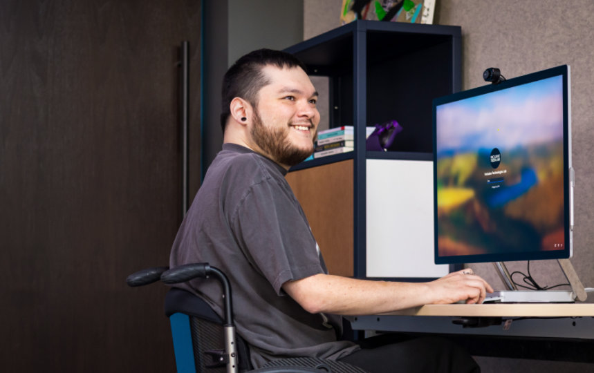 Una persona su una sedia a rotelle che sorride mentre lavora sul desktop.