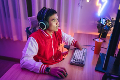 A male gamer with a physical disability is wearing a headset and playing online games in a neon-lit room.