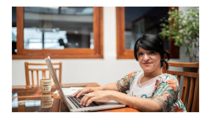 Mujer usando su ordenador con la oficina al fondo.