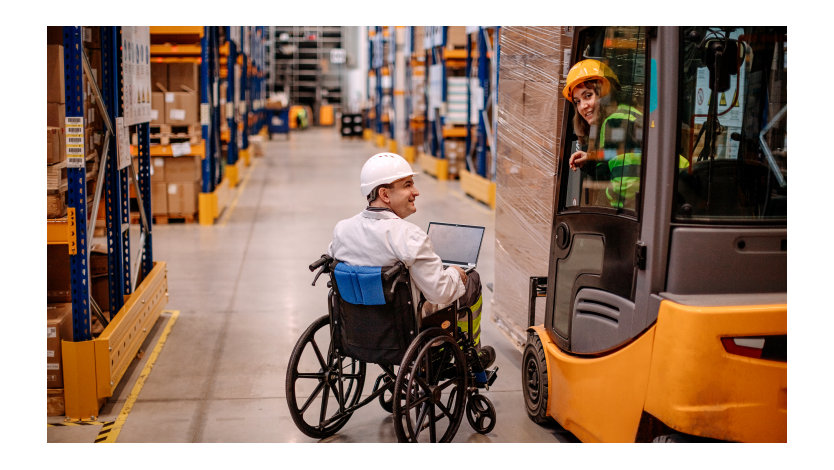 Un homme en fauteuil roulant utilisant un ordinateur et une jeune femme dans un chariot élévateur sourient en travaillant dans une usine.