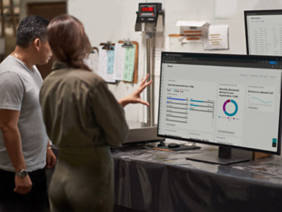 Two professionals analyzing data on a computer screen in a warehouse setting.