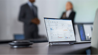 Un ordinateur portable est posé sur un bureau avec des personnes en arrière-plan.