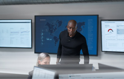 Skupiony mężczyzna stojący w centrum dowodzenia, w którym znajdują się ekrany z danymi i mapami.