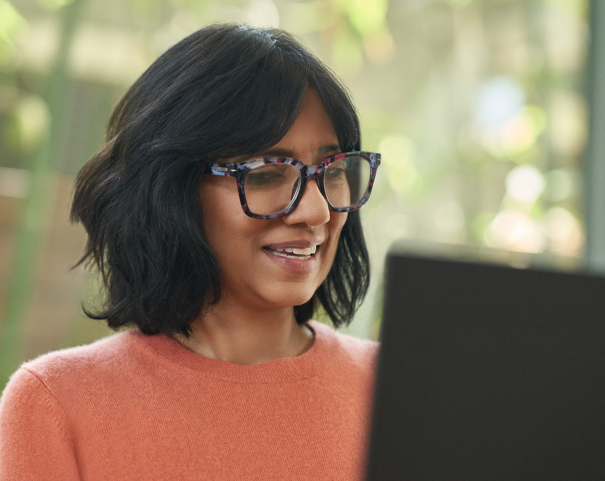 Eine Frau mit Brille lächelt und arbeitet an ihrem Laptop