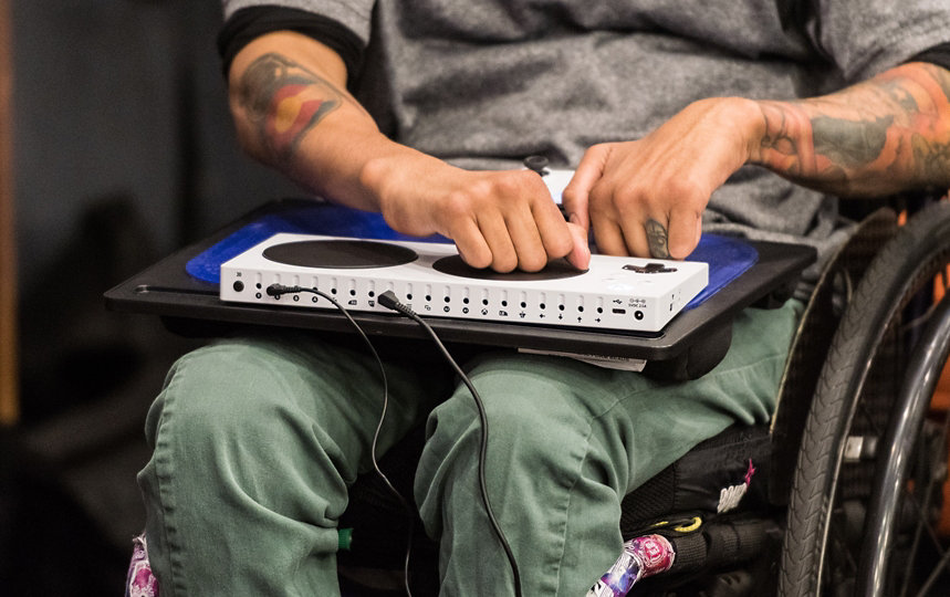 Une personne en fauteuil roulant utilise la manette Xbox Adaptive Controller.