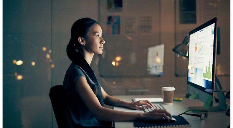 Pessoa a trabalhar num computador, num escritório com vidros, à noite.