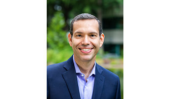 Person in a dark blue suit jacket and light purple shirt and smiling