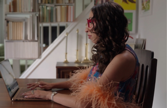 An image of a woman wearing fashionable clothing and accessories while working at a table using a Surface Laptop