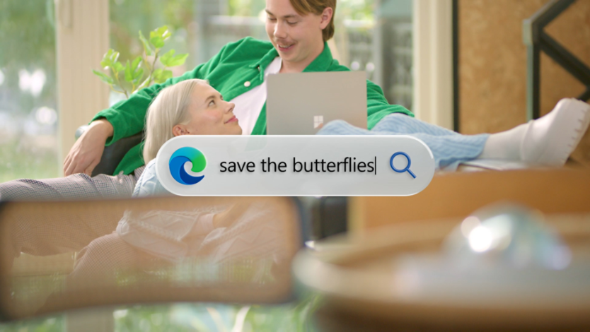A couple sitting on a couch while the woman holds a laptop on her lap. In the center of the image is a search bar with the edge icon on the left and the search bar text reads save the butterflies