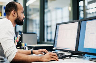 책상 앞에서 두 개의 모니터를 이용하여 일하고 있는 사람