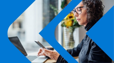 A person with one hand using a mobile phone and the other hand resting on a laptop.