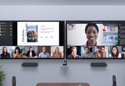 Zwei Fernseher nebeneinander, auf denen die Teilnehmenden eines Teams-Videochats zu sehen sind, und eine Präsentation, die während der Besprechung gehalten wird.