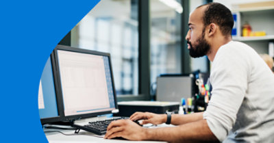 A person working at their desk looking at data in Microsoft Excel on a desktop monitor.