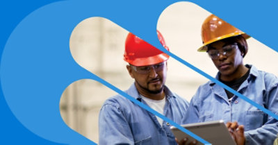 Dos trabajadores industriales con uniformes y cascos mirando una tableta.
